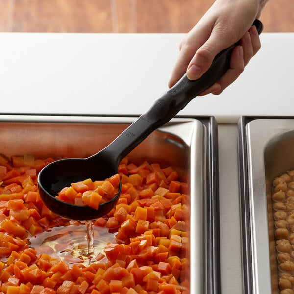 A hand holding a black Vollrath Spoodle pouring food into a container.