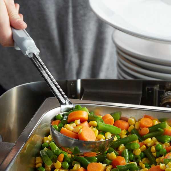 A hand using a Vollrath spoodle to serve vegetables from a pan.
