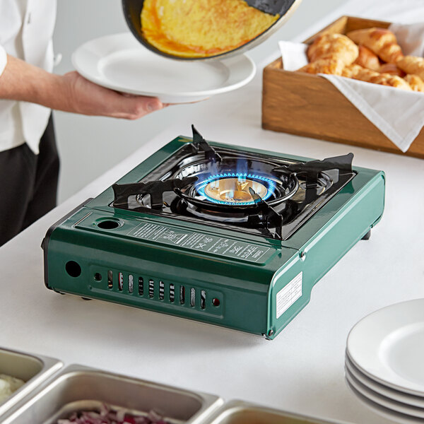 A person holding a plate of food over a flame on a Choice Green portable gas stove.