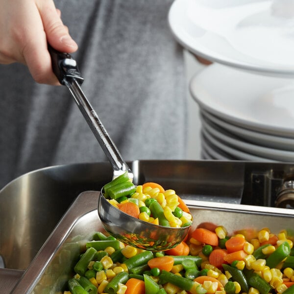 A hand using a Vollrath black perforated portion spoodle to serve vegetables