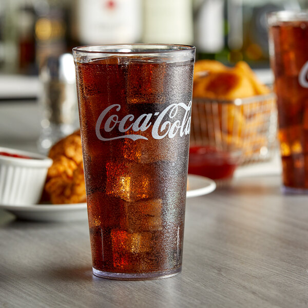 A clear plastic GET Coca-Cola tumbler filled with soda and ice on a table.