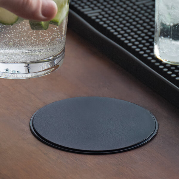 A hand holding a glass of water with a blue H. Risch, Inc. coaster on a table.