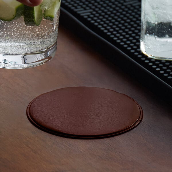 A hand placing a H. Risch, Inc. customizable coaster under a glass of water on a table.