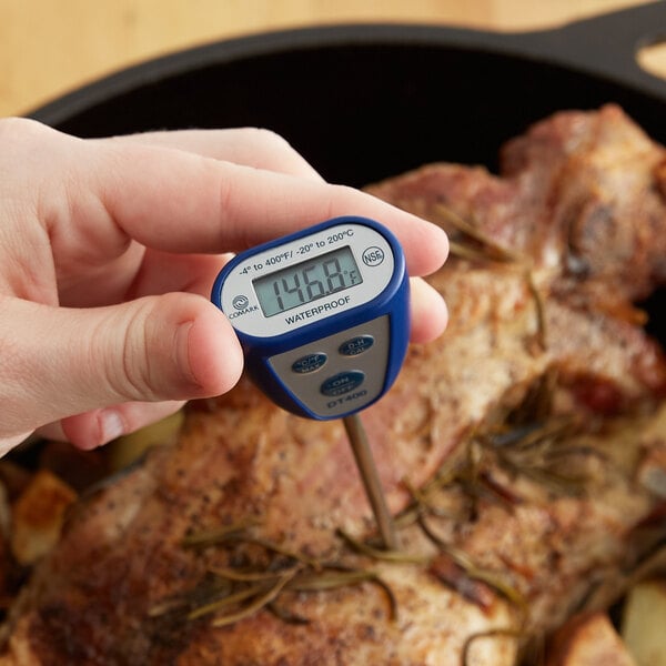 A person holding a Comark blue digital pocket probe thermometer to measure the temperature of a meat.