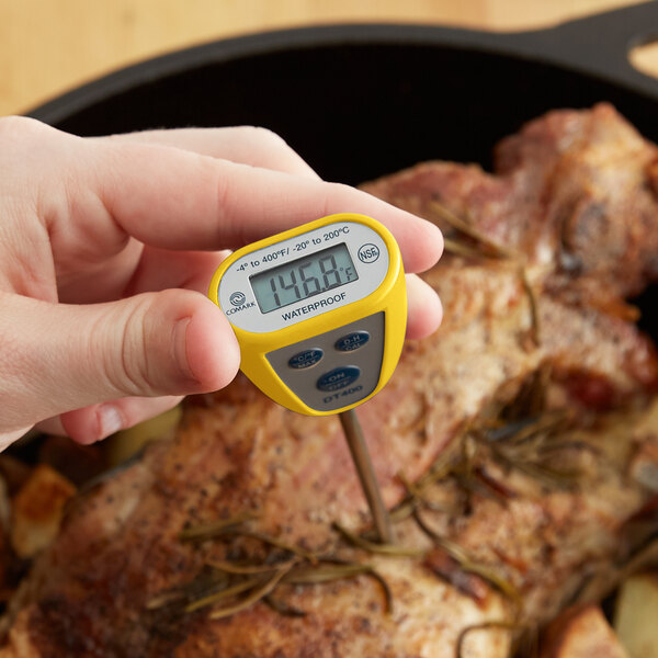 A hand holding a yellow and grey Comark digital pocket probe thermometer.