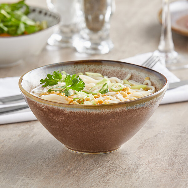 A Libbey Hedonite porcelain bowl filled with soup and noodles and green onions on a table.