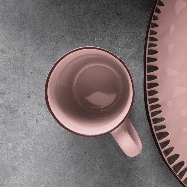 A Libbey pink stoneware mug next to a pink plate on a grey surface.