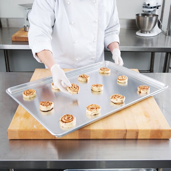 A person putting cinnamon rolls on a Chicago Metallic wire-in-rim baking sheet.