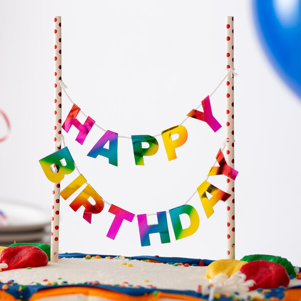 A white birthday cake with a "Happy Birthday" banner with colorful letters on it.