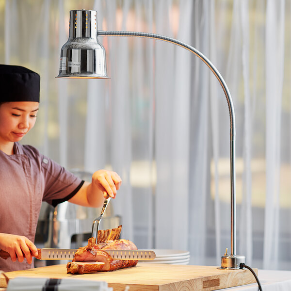 A woman using an Avantco single arm bulb warmer to cut food on a cutting board.