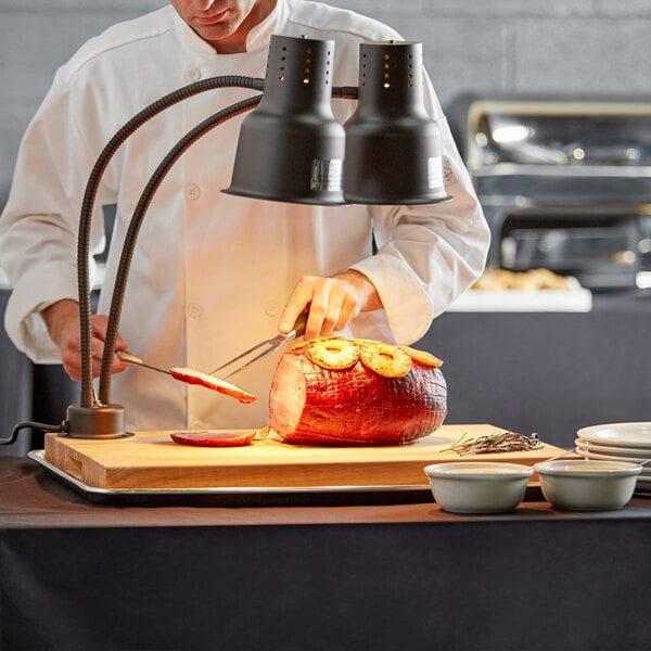 An Avantco chef using a carving station to cut a piece of meat.