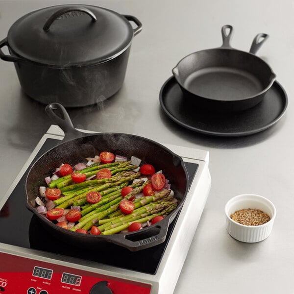 A Lodge cast iron skillet with asparagus and tomatoes cooking on a stove.