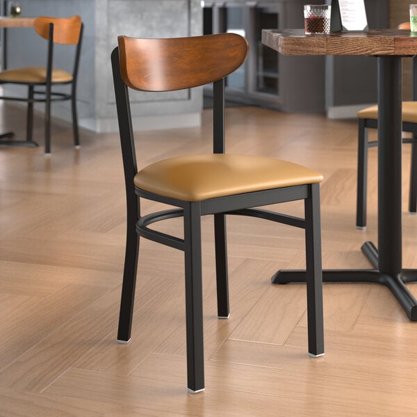 A Lancaster Table & Seating Boomerang chair with a light brown vinyl seat and antique walnut back on a table in a restaurant dining area.