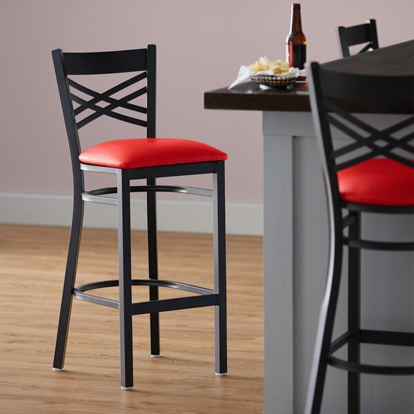 A Lancaster Table & Seating black cross back bar stool with a red vinyl padded seat.