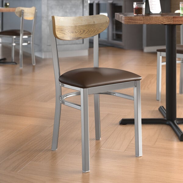 A Lancaster Table & Seating Boomerang Series chair with a driftwood back, clear coat finish, and dark brown vinyl seat in a restaurant.