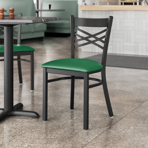 A black Lancaster Table & Seating cross back chair with a green vinyl padded seat at a table in a restaurant.
