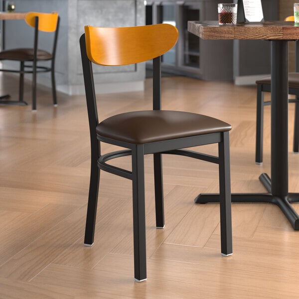 A Lancaster Table & Seating Boomerang Series Black Finish Chair with Dark Brown Vinyl Seat and Cherry Wood Back on a table in a restaurant.