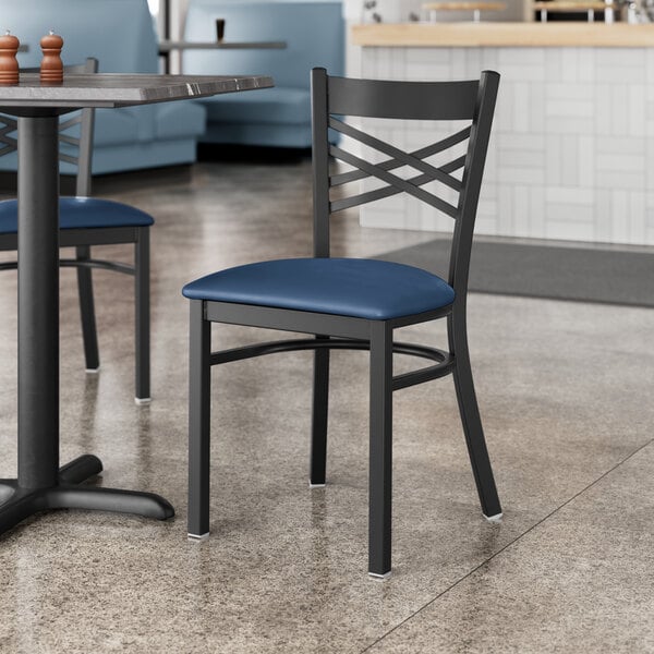 Two Lancaster Table & Seating black cross back chairs with blue vinyl padded seats at a table in a restaurant.