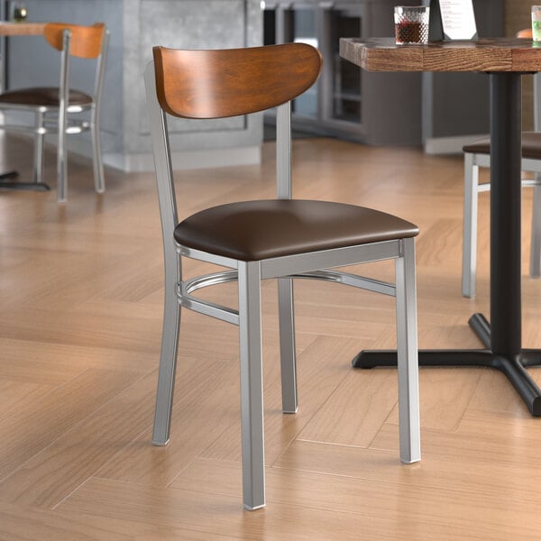 A Lancaster Table & Seating Boomerang Series chair with a dark brown vinyl seat and antique walnut wood back in a restaurant.