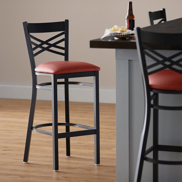 A Lancaster Table & Seating black cross back bar stool with burgundy vinyl seat.