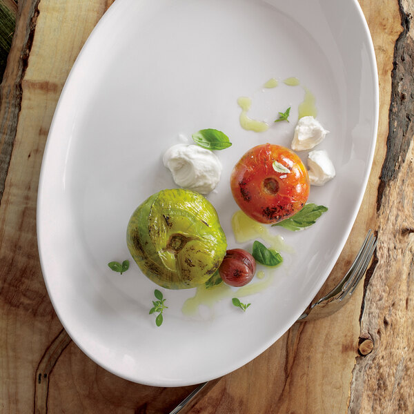 A Oneida Royale bright white porcelain winged platter with tomatoes, cheese, and herbs on a wooden surface.