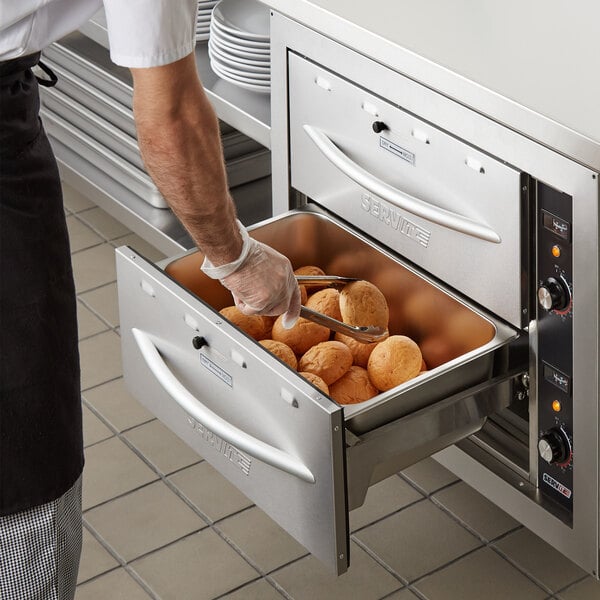 A man using a ServIt built-in drawer warmer to heat bread in a metal container.