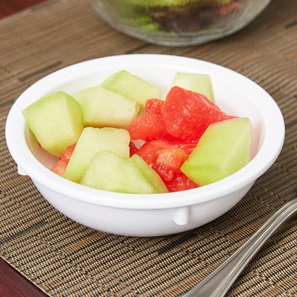A Carlisle white melamine nappie bowl filled with sliced watermelon on a table.
