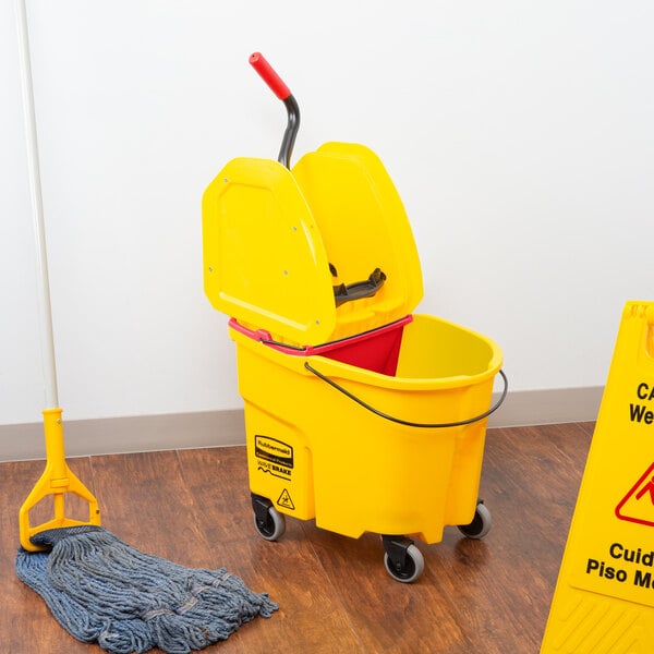 A Rubbermaid yellow mop bucket with a red wringer next to a yellow caution sign.