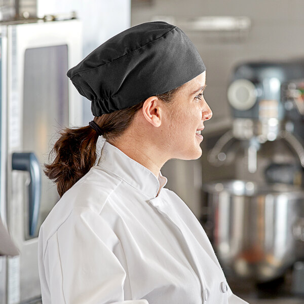 A woman in a chef's uniform wearing a black Choice top chef hat with a black border.