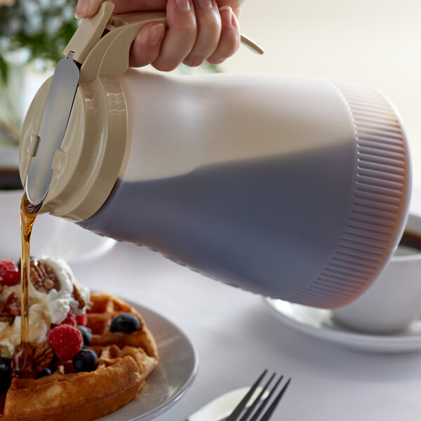 A hand using a Vollrath Dripcut server to pour syrup onto a waffle.