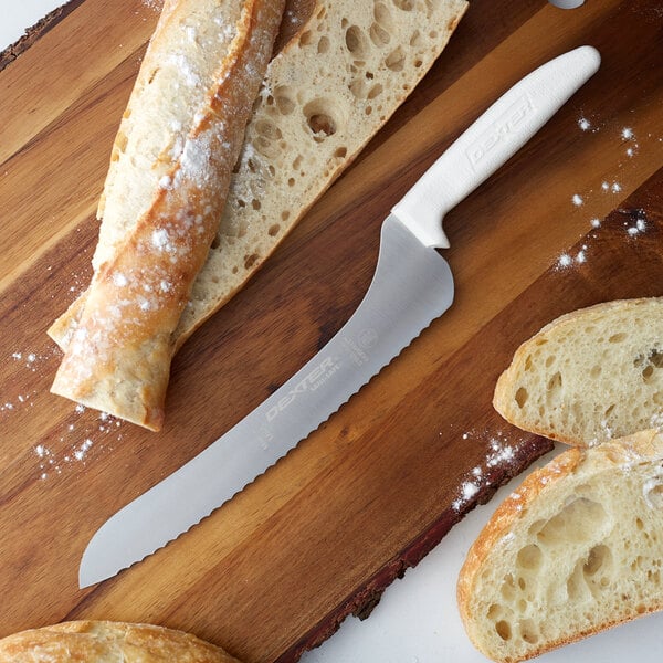 A Dexter-Russell scalloped bread knife next to a piece of bread on a cutting board.