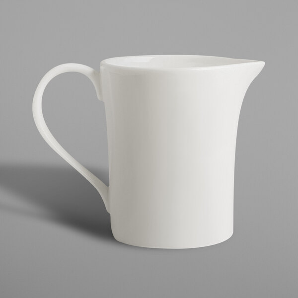 A white porcelain creamer pitcher with a handle.