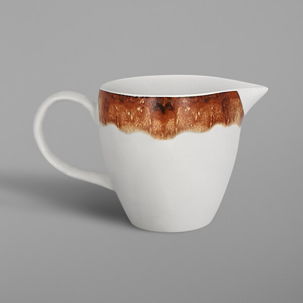A white porcelain creamer with brown paint on the rim.