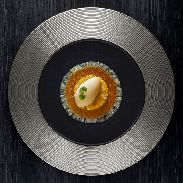 A RAK Porcelain metal fusion flat plate with food on it on a black surface.