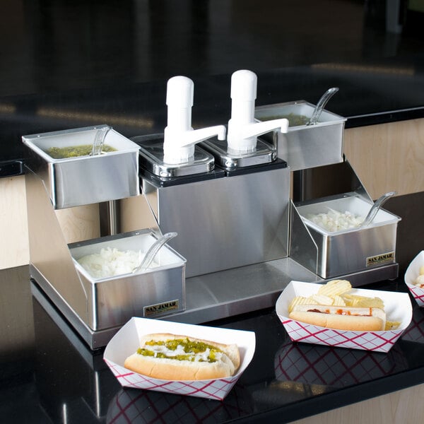 A San Jamar dual pump condiment system on a counter with a hot dog and other food items.