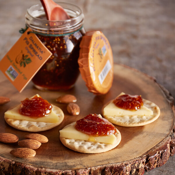 A wood slab with Dalmatia Original Fig Spread on crackers with cheese and nuts.