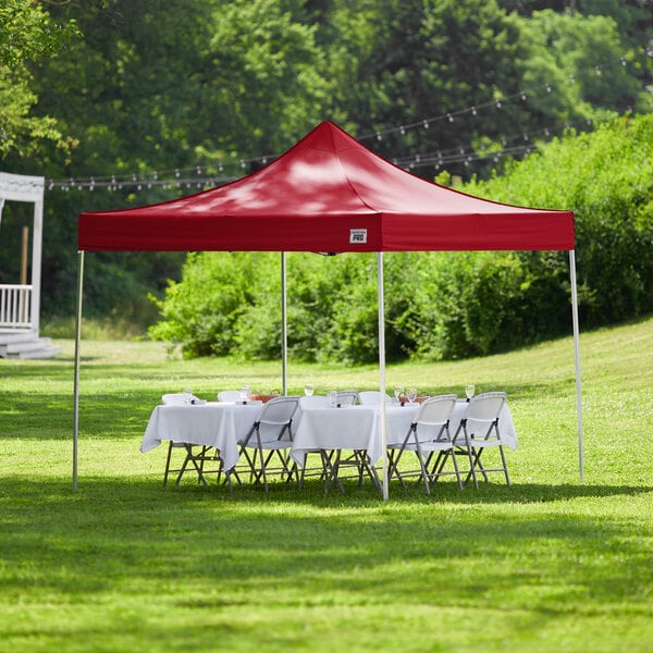 A red Backyard Pro Courtyard Series canopy tent set up on a grassy area with a table and white tablecloth.