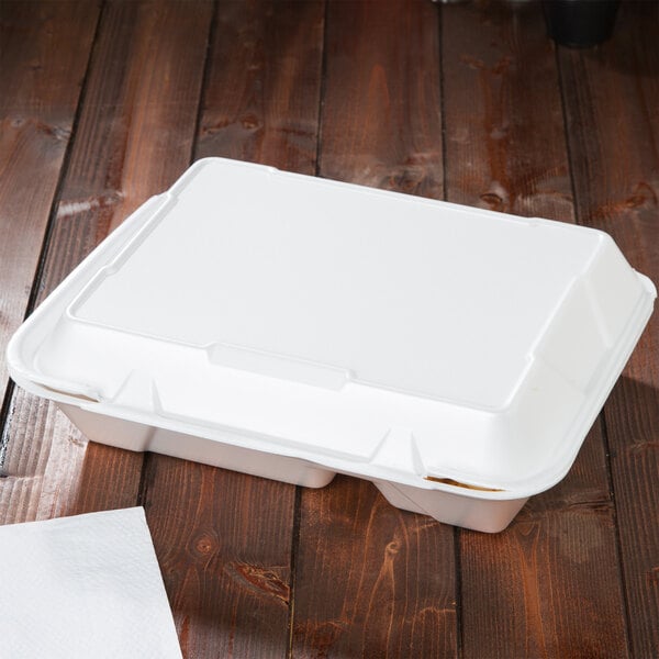 A white Genpak foam container with hinged lid on a wood surface.