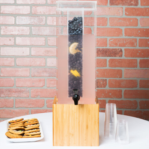 A Cal-Mil bamboo infusion dispenser with a black faucet on a wooden pedestal.