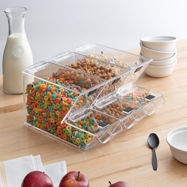 A Choice stackable plastic container with cereal in it on a table with a white bowl and red apple.