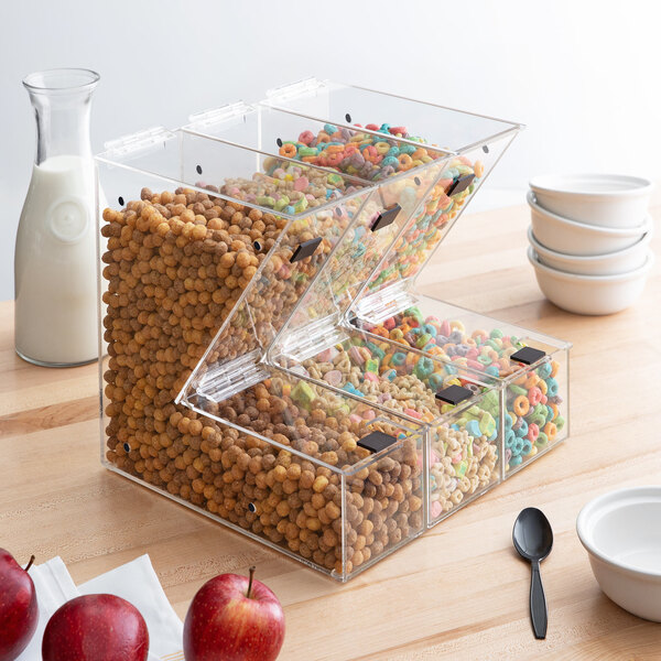 A stack of clear plastic cereal dispensers with notches filled with cereals and apples.