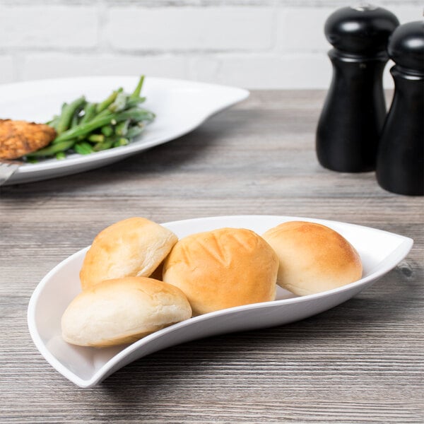 A white GET San Michele melamine bowl filled with bread rolls and green vegetables on a table.