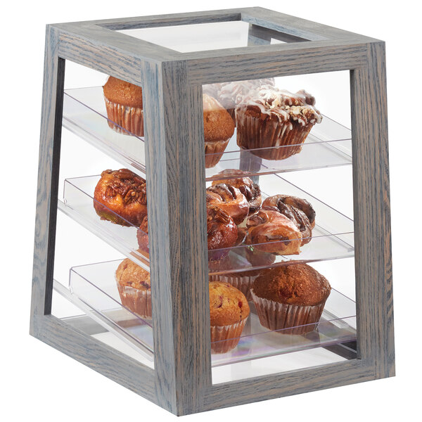A Cal-Mil Ashwood Gray Oak 3-tier display case with muffins and cupcakes on a table.