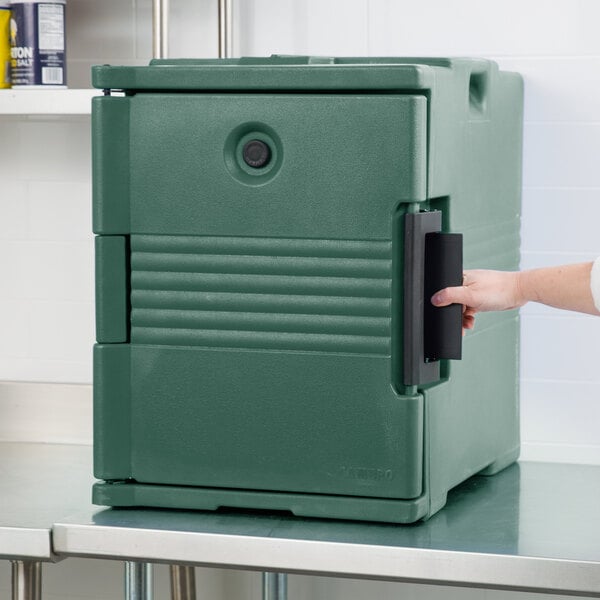 A hand opening the front of a green Cambro Ultra Pan Carrier.