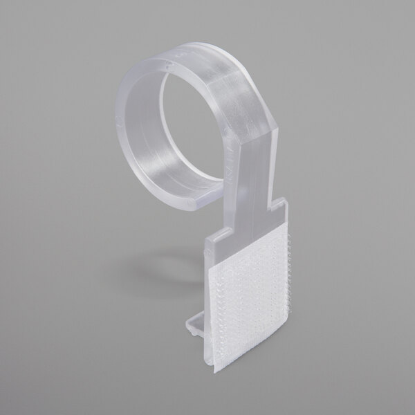A clear plastic table skirt clip with white hook and loop attachment.