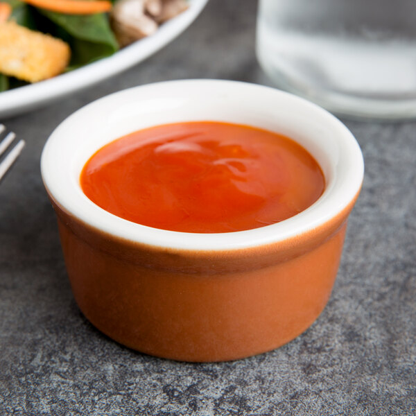 A Tuxton Autumn white china ramekin filled with red sauce on a table next to food.