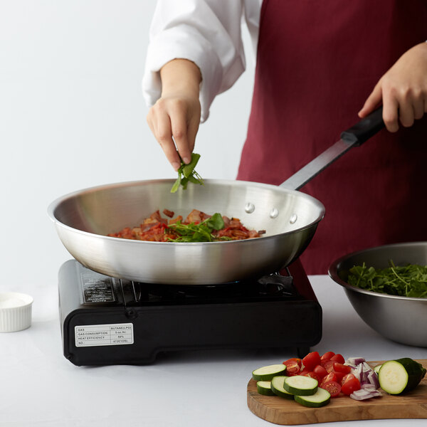 A woman cooking vegetables in a Choice aluminum fry pan with a black silicone handle.