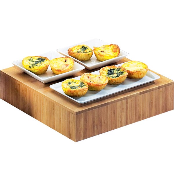 A Cal-Mil bamboo square riser with four mini quiches on it.