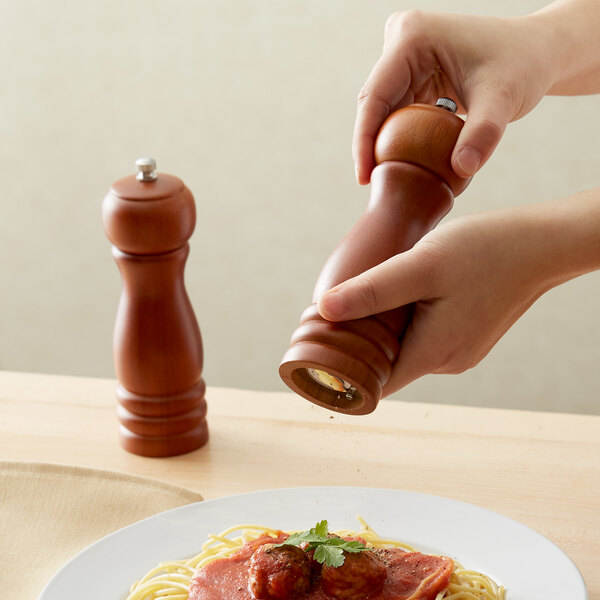 A person using an Acopa brown wooden pepper mill to season spaghetti with meatballs.