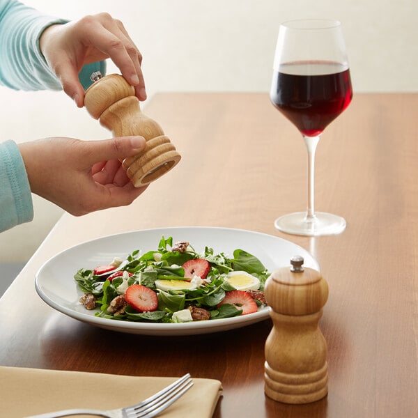A person using a wooden Acopa pepper mill to season a salad.